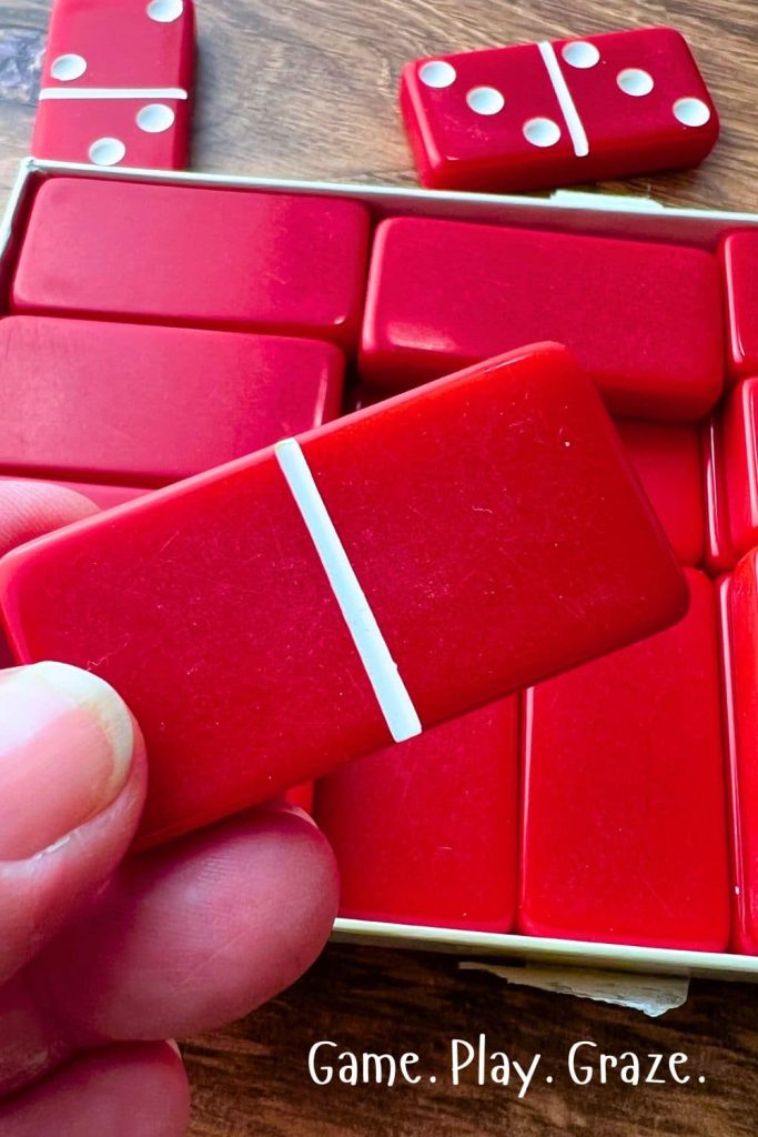 HOW TO PLAY DOMINOES What Is A Blank Domino Tile Scoring Blank Dominoes - hand holding a red blank domino with no pips dots